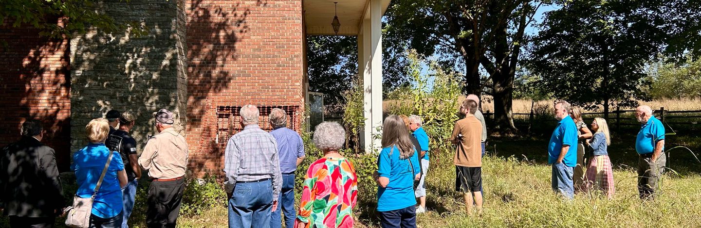 A group gathered outside the house, looking at the brick wall where the work is under way.