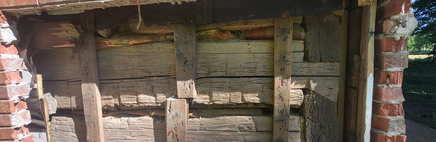 Hand hewn logs exposed where the brick veneer has been taken off the wall.