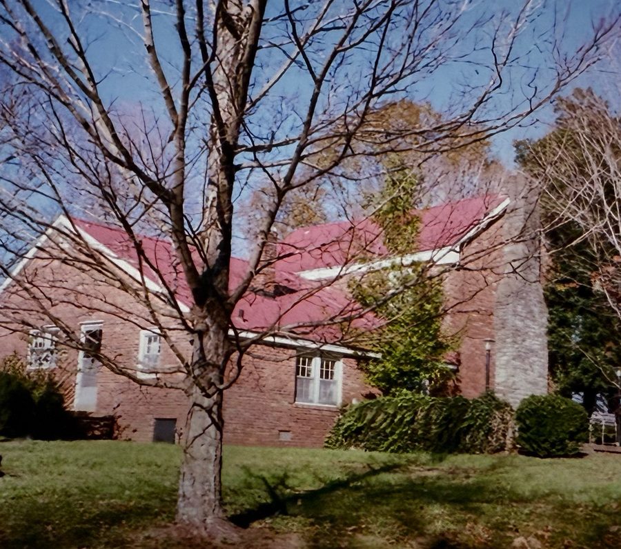 The brick house with its red roof, seen from the yard through a bare tree.