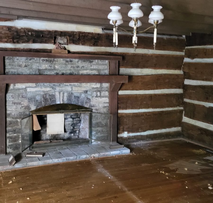 The stone fireplace in a log wall, its mantel and chimney breast intact.