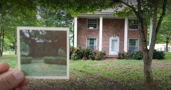 A hand holds a faded, undated print up in front of the brick house.