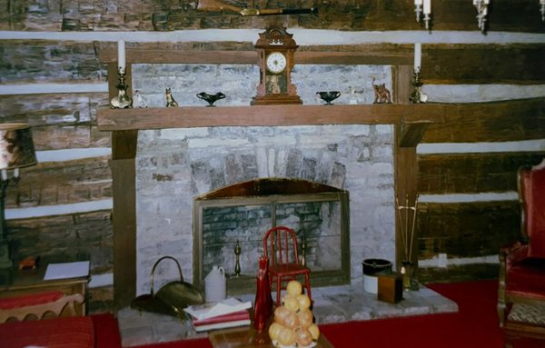 The stone fireplace and mantel inside the house, with a clock and ornaments on the shelf.