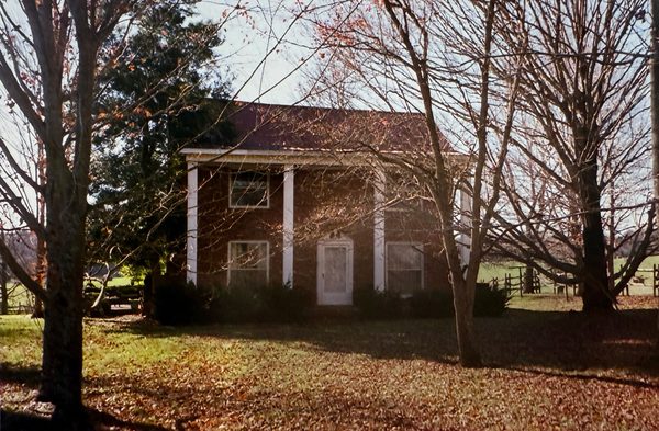 The brick house in late autumn, seen through bare trees.