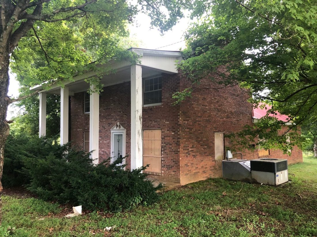 The side of the house under its brick veneer, the ground around it overgrown.