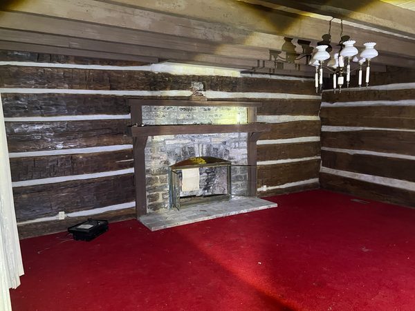 A room with red carpet and a stone fireplace, the log walls whitewashed between the courses.