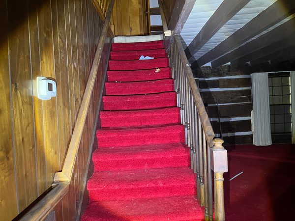 A staircase with red carpet, the walls panelled in wood.