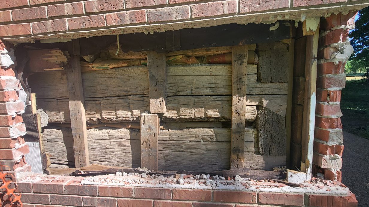 Hand hewn logs and a heavy header beam, exposed where the brick has been opened.